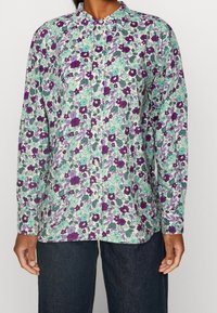 Pitkähiha paita kukkakuosilla, jossa violetteja, teal ja mintunvihreitä sävyjä. Siinä on napitettava kaulus ja suora helma.