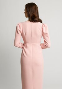 Różowa sukienka z długim rękawem, z bufkami na ramionach i dopasowaną sylwetką. Posiada zamek błyskawiczny z tyłu oraz gładką teksturę materiału.