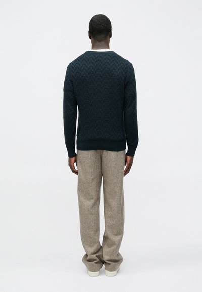 Pull texturé bleu marine avec un col clair contrastant, associé à un pantalon large marron clair et des baskets blanches.