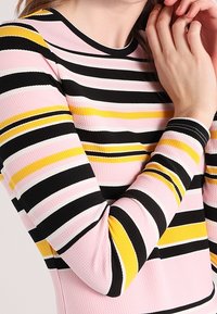 Maglietta a maniche lunghe con strisce orizzontali in rosa, nero, giallo e bianco. Tessuto strutturato con scollatura rotonda.