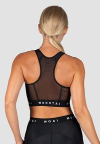 Juoda sportinė liemenėlė su tinkleliu nugaros dalyje, plačiomis petnešėlėmis ir elastinga juosta su "MOROTAI" logotipu. Lygi medžiaga ir prigludęs dizainas sportinei aprangai.