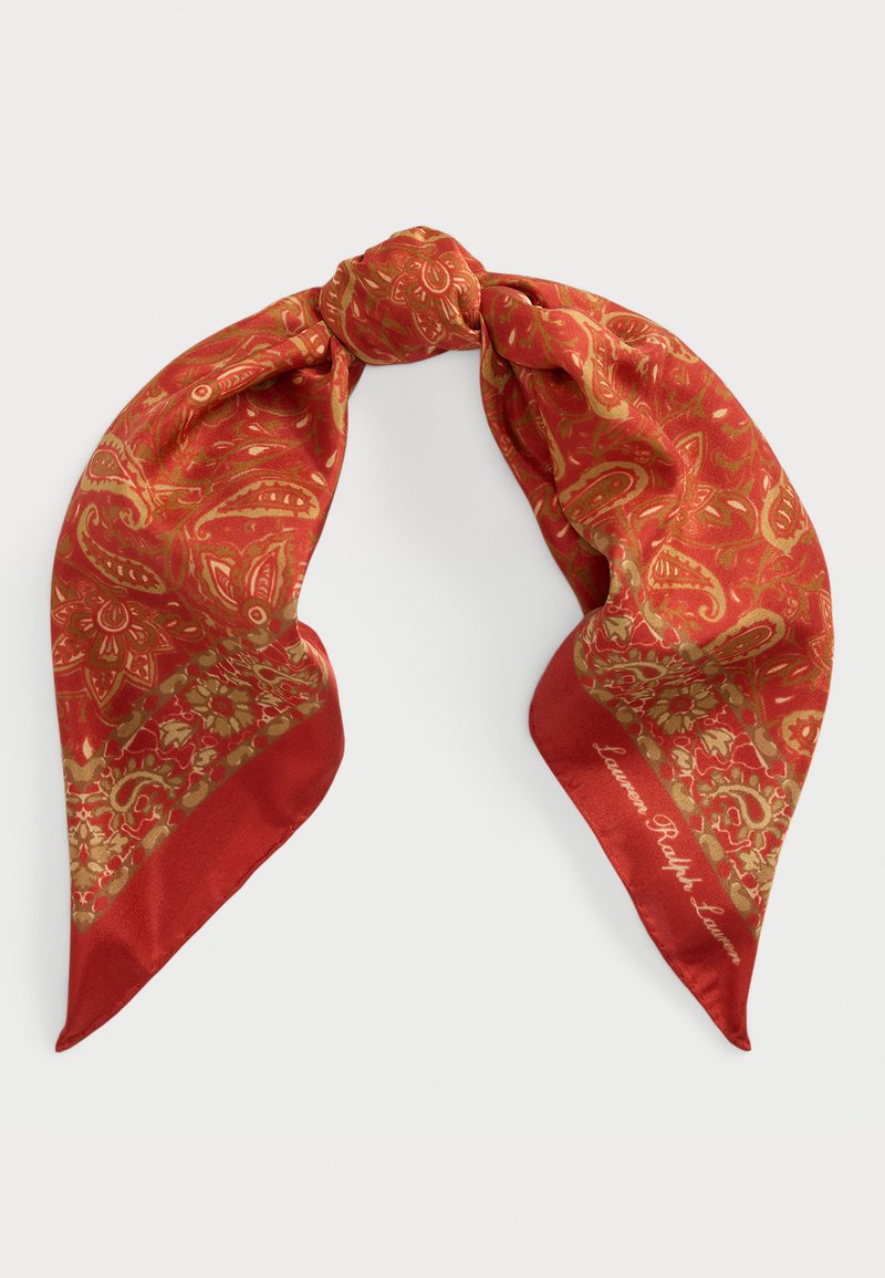 Silk scarf in vibrant red with gold paisley pattern. Features a knotted design with pointed ends. Signature text on one side.