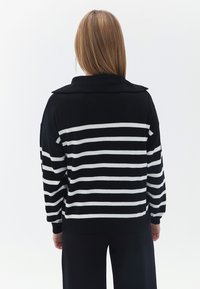 Schwarz-weißer gestreifter oversize Pullover mit Kragen und langen Ärmeln, ausgestattet mit gerippten Bündchen und Saum. Glatte Textur.