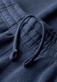 Mørkeblå træningsbukser har en tekstureret talje med samlet detalje og snøre. Materialet ser blødt og let børstet ud.