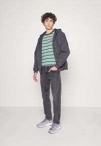 Grijze denimjas met een capuchon, gestreept groen en zwart T-shirt, grijze spijkerbroek en grijze sneakers. Minimalistisch ontwerp met zichtbare texturen.