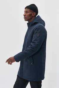 Chaqueta impermeable azul marino con capucha, con cremallera en la parte delantera y bolsillos laterales. Textura suave, con un parche de logo en la manga.