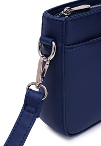 Tmavě modrá kožená kabelka má kovový zip, lesklé stříbrné kovové doplňky, odnímatelný popruh a čisté, strukturované okraje.