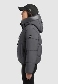 Pūkaina pelēka jaka ar kapuci, ar rāvējslēdzēju un sānu kabatām. Satur melnu logotipa uzlīmi uz piedurknes un ribotu aproci. Valbā tumša cepure.