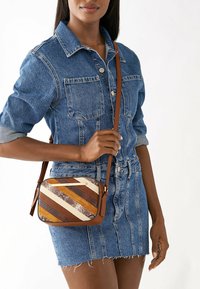 Sac bandoulière avec une bandoulière en cuir marron, présentant un design rayé dans des tons beige, marron et or. Surface texturée et forme rectangulaire.