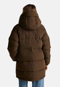 Hnědá puffrová bunda s kapucí, s prošívaným designem, viditelným šitím a středně dlouhým střihem, doplněná elastickými manžetami.