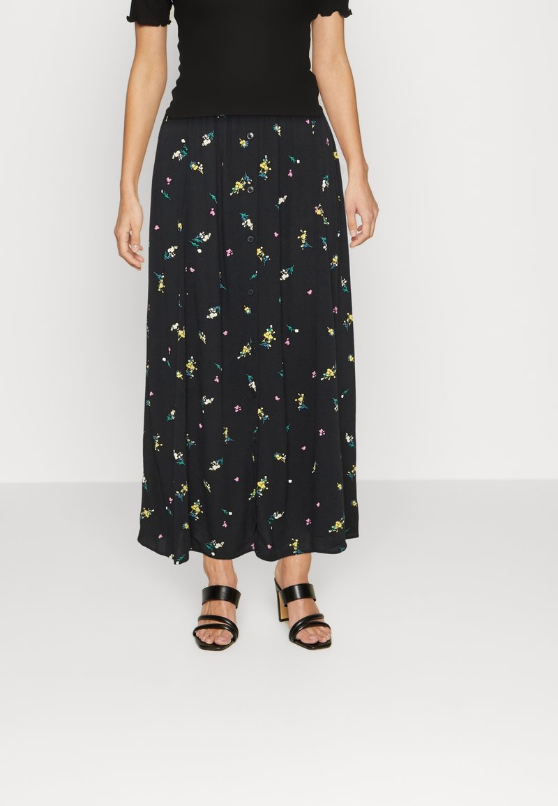 Jupe maxi noire à motifs floraux, avec un devant à boutons, des motifs floraux colorés, un tissu fluide et une coupe décontractée. Associée avec des sandales noires.