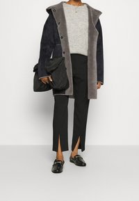 Lungo cappotto blu navy con rivestimento grigio, maglione grigio a maglia, pantaloni neri con spacchi laterali, mocassini neri con hardware dorato, borsa a spalla nera.