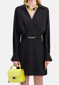 Svart långärmad omslagsklänning med ett silverkedjebälte, matchad med en gul strukturerad handväska och ett blommigt halsband i klara färger.