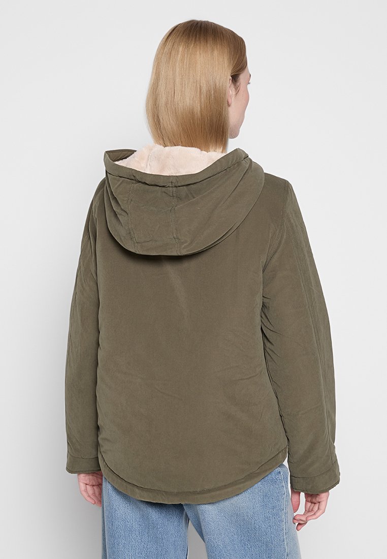 Giacca a cappuccio verde oliva con un morbido rivestimento interno beige, caratterizzata da un orlo arrotondato e un taglio casual. Realizzata in un tessuto liscio e testurizzato.