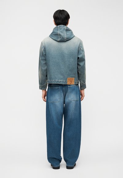 Τζιν μπουφάν με κουκούλα, ανοιχτό έως σκούρο λευκό προς μαύρο βαθμιαίο χρώμα, με ωμές άκρες, συνδυασμένο με άνετο, φαρδύ παντελόνι τζιν. Ετικέτα στο πίσω μέρος του μπουφάν.