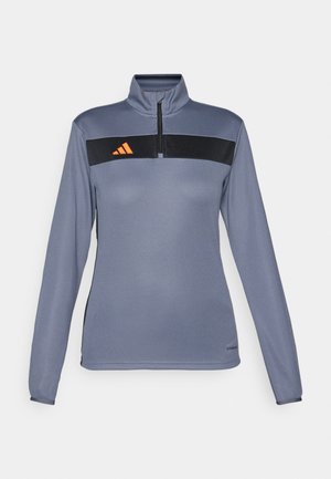 Svetlo siva dolgī rokav športna majica s pol-zadrgo na ovratniku, ki ima črno vodoravno črto in oranžni logotip na prsih. Gladka tekstura tkanine.