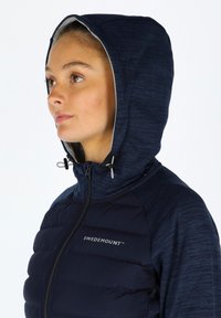Marineblauwe gewatteerde jas met een capuchon, met een gestructureerd bovenstuk en een gladde onderpaneel. Zilveren merklogo op de borst.