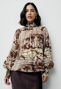 Bruine en roze gebloemde blouse met een hoge hals, geplooide details en lange ballonmouwen. Gemaakt van lichtgewicht stof met een soepele textuur.