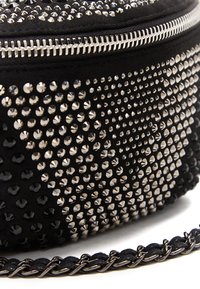 Zwarte ronde tas met zilveren studs en strass, met een ritssluiting en een gevlochten schakelkettinkje om te dragen. Zachte textuur.