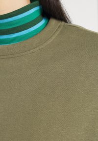 Felpa in cotone verde oliva con colletto alto e righe orizzontali verdi e blu. Texture liscia, design casual.