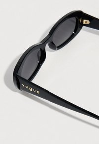 Μαύρα γυαλιά ηλίου με γυαλιστερό φινίρισμα, με σκουρόχρωμους φακούς και την επωνυμία «vogue» σε χρυσό στο πεταλούδα. Γωνιώδης σχεδίαση, ανθεκτικοί σκελετοί.