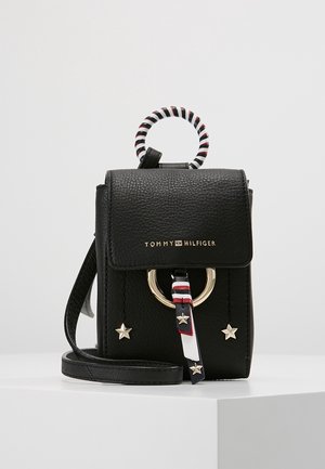 Lille sort læder Tommy Hilfiger crossbody-taske med gyldne stjerner, en gylden ring og et sort, hvidt og rødt stribet håndtag.