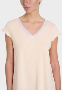 Top pesca chiaro a scollo a V con maniche a cappuccio. Il tessuto morbido presenta un bordo bianco in contrasto attorno al collo, creando un sottile dettaglio di accento.