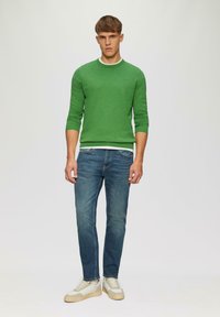 Groene ronde hals trui met driekwart mouwen, gecombineerd met blauwe jeans en witte sneakers. De trui heeft een zachte textuur en een ribgebreide zoom.