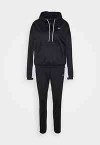 Ensemble de survêtement Reebok noir et blanc avec sweat à capuche et pantalon de jogging assorti, présentant des détails de logo sur la poitrine et la jambe.