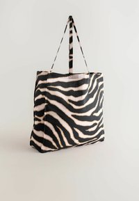 Sort og beige zebra-stribede tote taske med lange håndtag, stående oprejst mod en ensfarvet lys baggrund.