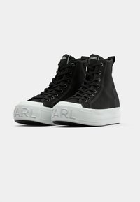 Μαύρα ψηλά αθλητικά παπούτσια από καμβά με παχύ λευκό καουτσούκ σόλα, που διαθέτει ανυψωμένο λογότυπο στο εμπρόσθιο μέρος και μαύρα κορδόνια.