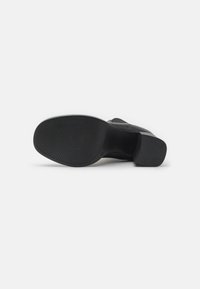 Suela de zapato negra con superficie texturizada, tacón ligeramente elevado y forma redondeada. Sin marcas visibles ni elementos decorativos.