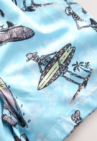 Light blue fabric with a playful print featuring skeletons on surfboards, tropical palms, and patterned accents. Smooth texture; casual design.