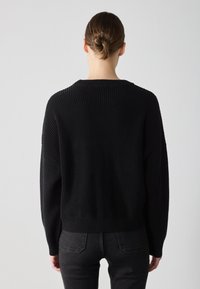 Svart strikket genser med ribbestruktur, løs passform og bred rund hals. Overdimensjonerte ermer og nederkant designet for komfort.