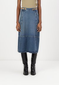 Denim midi-skjørt med rett snitt, lyseblå farge og kontrastsøm. Har belte i midjen med brune detaljer. Brukt med svarte støvler.