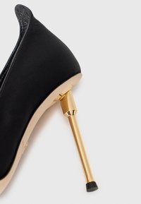Black satin high-heeled shoe with a metallic gold stiletto heel and a rounded toe. Smooth texture with a glossy accent along the edge.