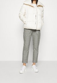 Luddig krämfärgad jacka med stor krage, i kombination med grå rutiga byxor och vita sneakers. Outfiten har en sportig look.