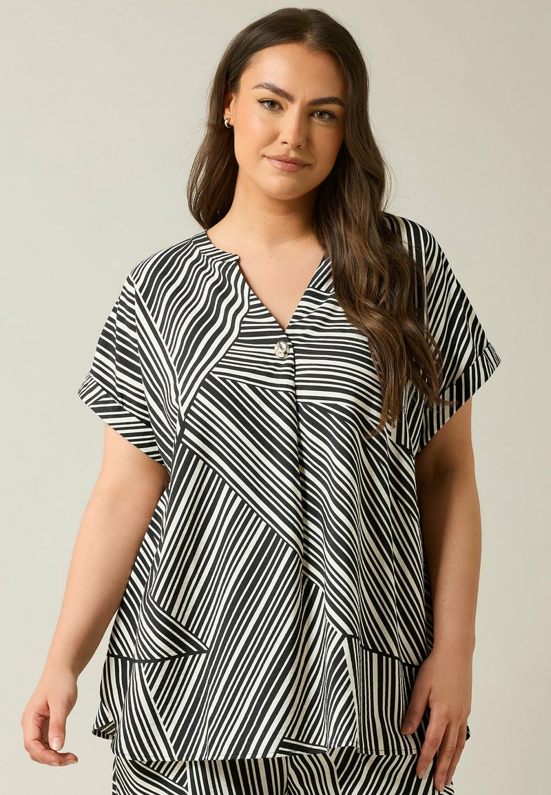 Blusa a righe bianche e nere con scollatura a V, maniche corte e vestibilità ampia, caratterizzata da un bottone decorativo all'collo.
