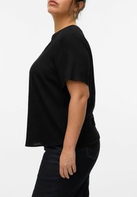 Camiseta negra de manga corta con un corte relajado, hecha de material suave, con cuello redondo y un diseño con aberturas laterales. Combinándola con unos vaqueros oscuros.
