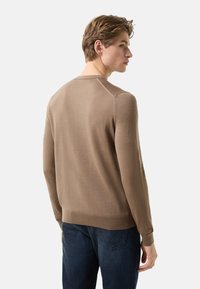 Brown ribbed knit sweater with long sleeves, round neckline, and contrasting cuffs; styled with dark blue jeans and a smooth texture.