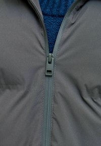 Giacca grigia con cerniera, con interno in pile blu navy strutturato. Include una robusta cerniera con tirante in plastica per una facile chiusura.