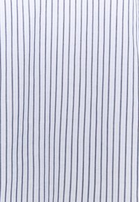 Tissu blanc avec des rayures verticales bleu marine, doté d'une finition texturée. Les rayures sont uniformément espacées, créant un motif régulier.