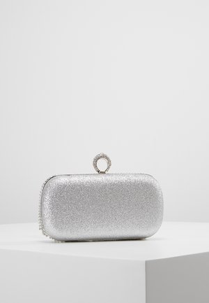 Rektangulær sølvglitter clutch med rundede kanter og en cirkulær rhinstenlås på toppen, placeret på en hvid piedestal.