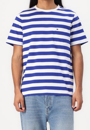 Person iført en blå og hvid vandret striped t-shirt med en brystlomme og lyseblå jeans.
