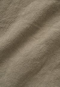 Tissu brun clair texturé avec un motif de tissage visible et des plis naturels créant des ombres douces et de la profondeur.