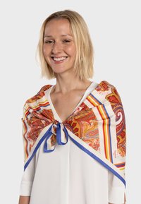 Écharpe en soie colorée avec des motifs complexes de paisley et de rayures, nouée avec un ruban bleu ; drapée sur un haut blanc. Texture lisse.