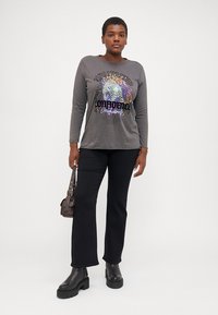 Grå långärmad graphic t-shirt med en färgglad djurprint och djärv text, kombinerad med svarta utsvängda byxor och kraftiga svarta stövlar.