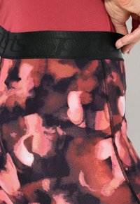 Zwarte elastische tailleband met de tekst "sports"; paars, roze en rood patroon; nauwsluitend atletisch ontwerp; naadloze zijkanten.