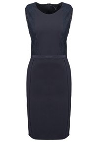 Marinblå klänning i fodral med spetsdetaljer på axeln, figursydd silhuett och mjuk textur. Bakre dragkedjestängning, knälång.