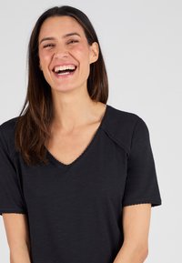 T-shirt nera con scollatura a V e maniche corte, bordi ondulati, realizzata in tessuto morbido, caratterizzata da una vestibilità comoda e dettagli di design minimal.